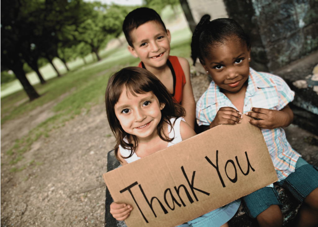 Tres niños sosteniendo un cartel que dice Gracias