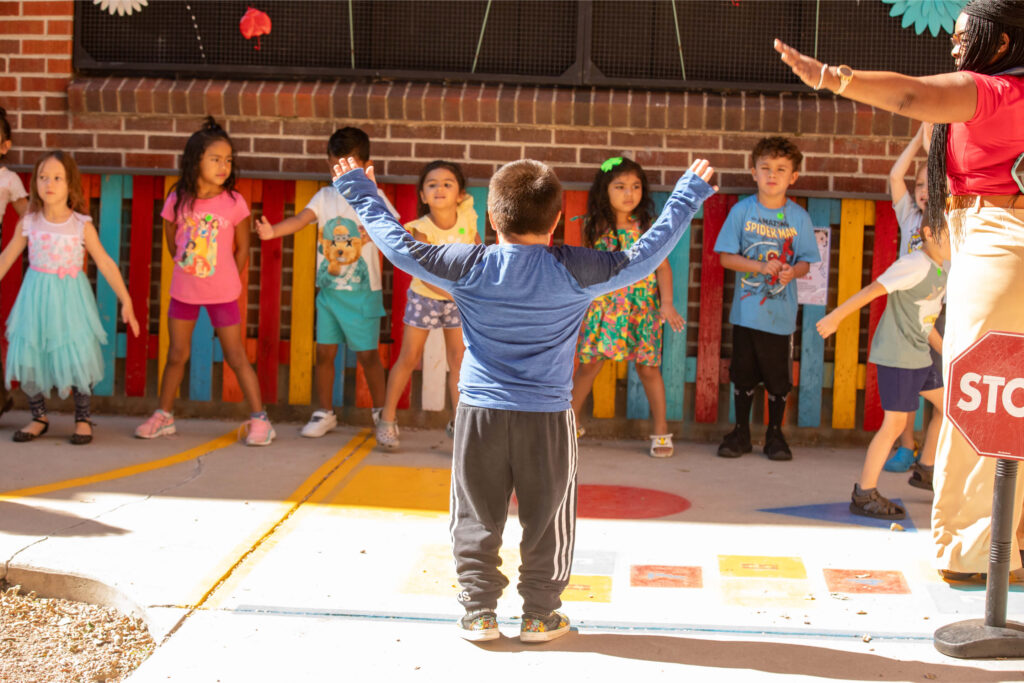 Menino com os braços levantados em frente à turma da pré-escola