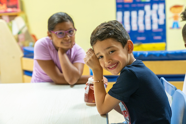 Menino em idade pré-escolar sorrindo para a câmera com uma menina ao fundo