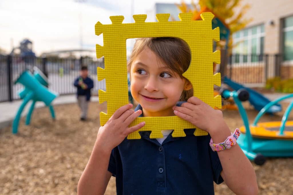 Fotografía de una niña mirando a través de una pieza de rompecabezas con forma de B