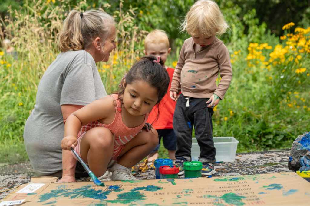 Tres niños de preescolar y una maestra pintando al aire libre