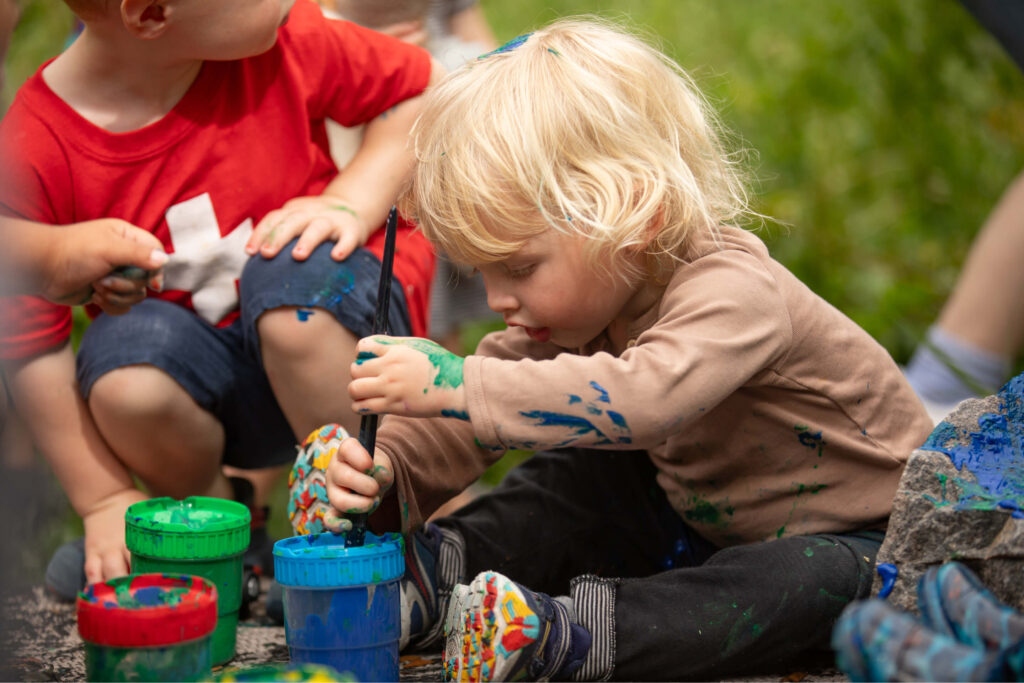 Un niño de preescolar y un compañero de clase juegan con pinturas de dedos al aire libre