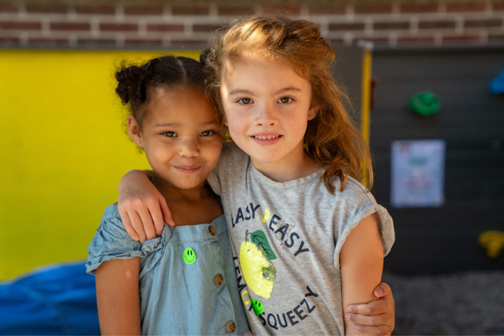 Dos niñas en edad preescolar con los brazos sobre los hombros de la otra