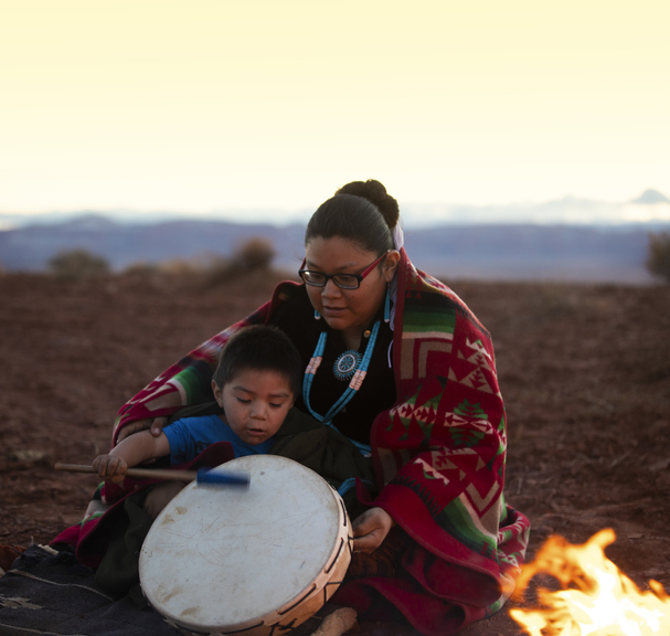 Mujer joven navajo con niño y tambor cerca de una fogata