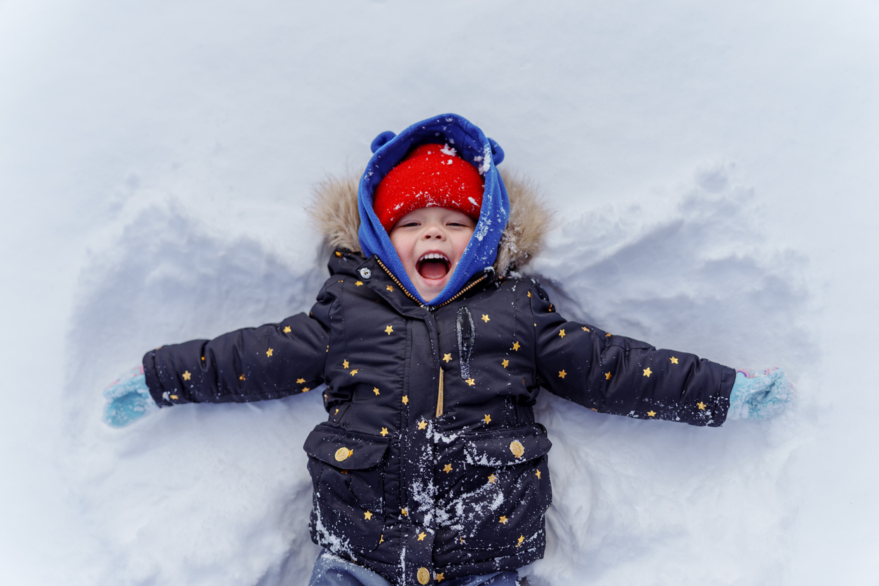 Un enfant d'âge préscolaire en manteau d'hiver fait des angles dans la neige