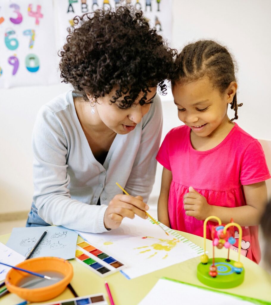 Mujer ayudando a niña de preescolar con proyecto