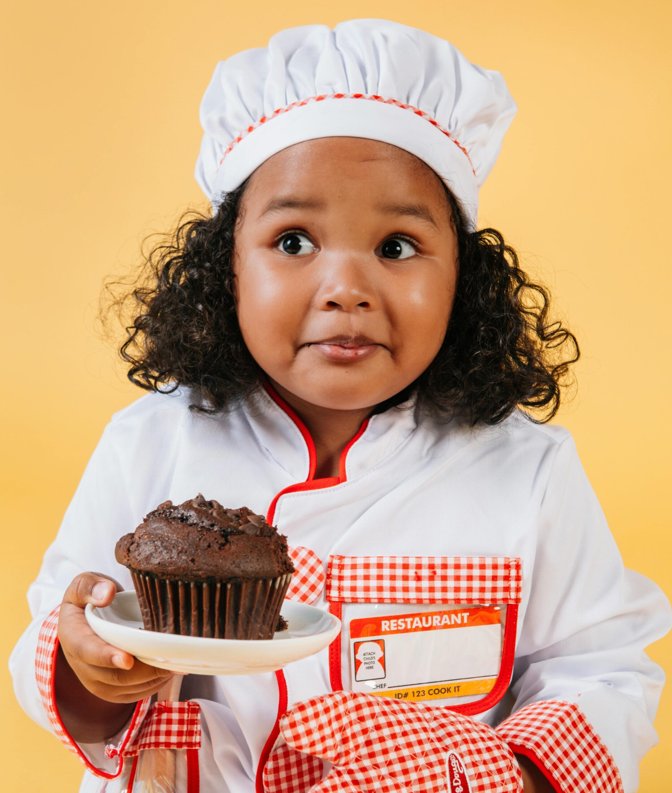 Girl in a chef's outfit holding a chocolate muffin