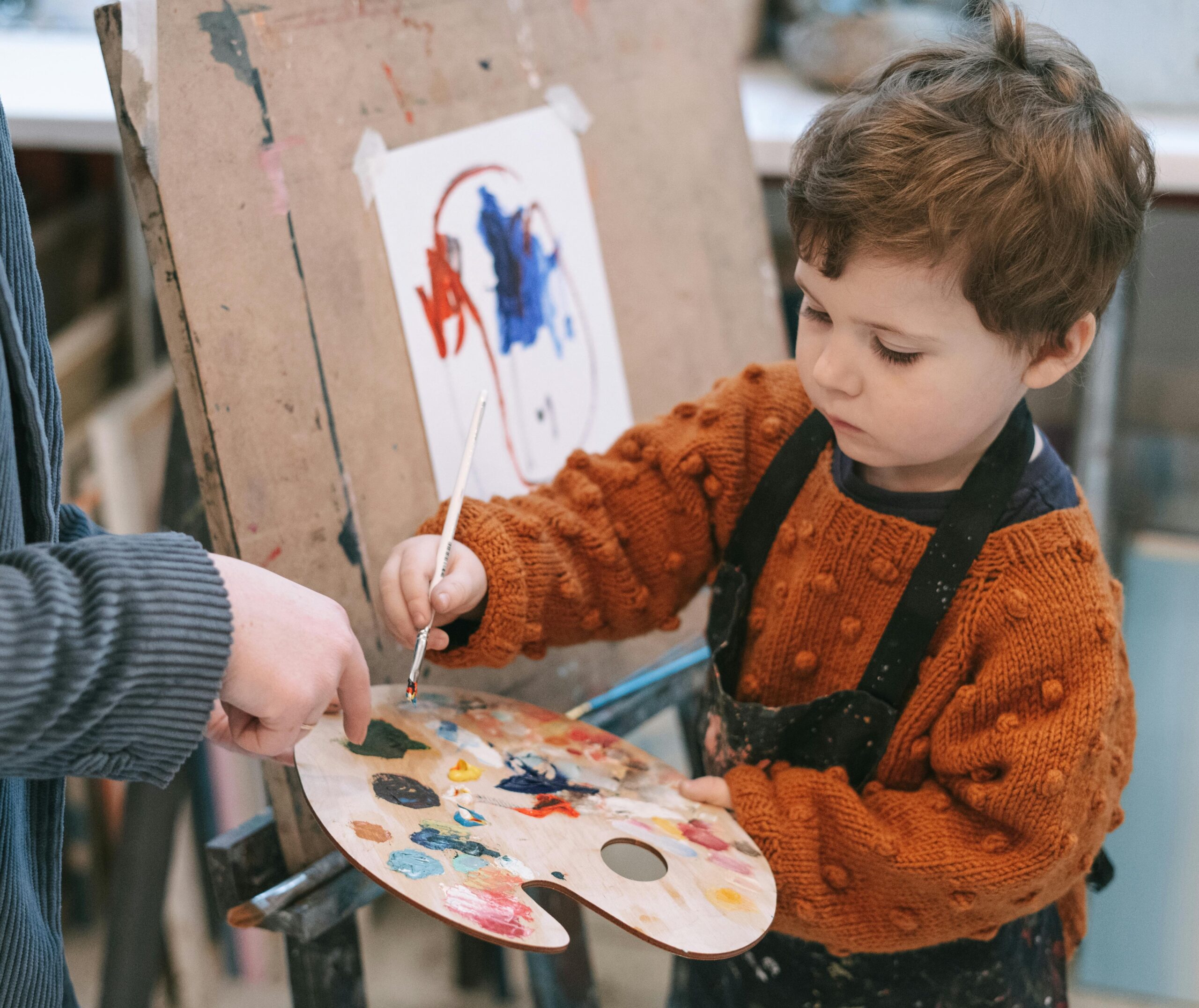 Young boy in apron dipping his paint brush in paint.