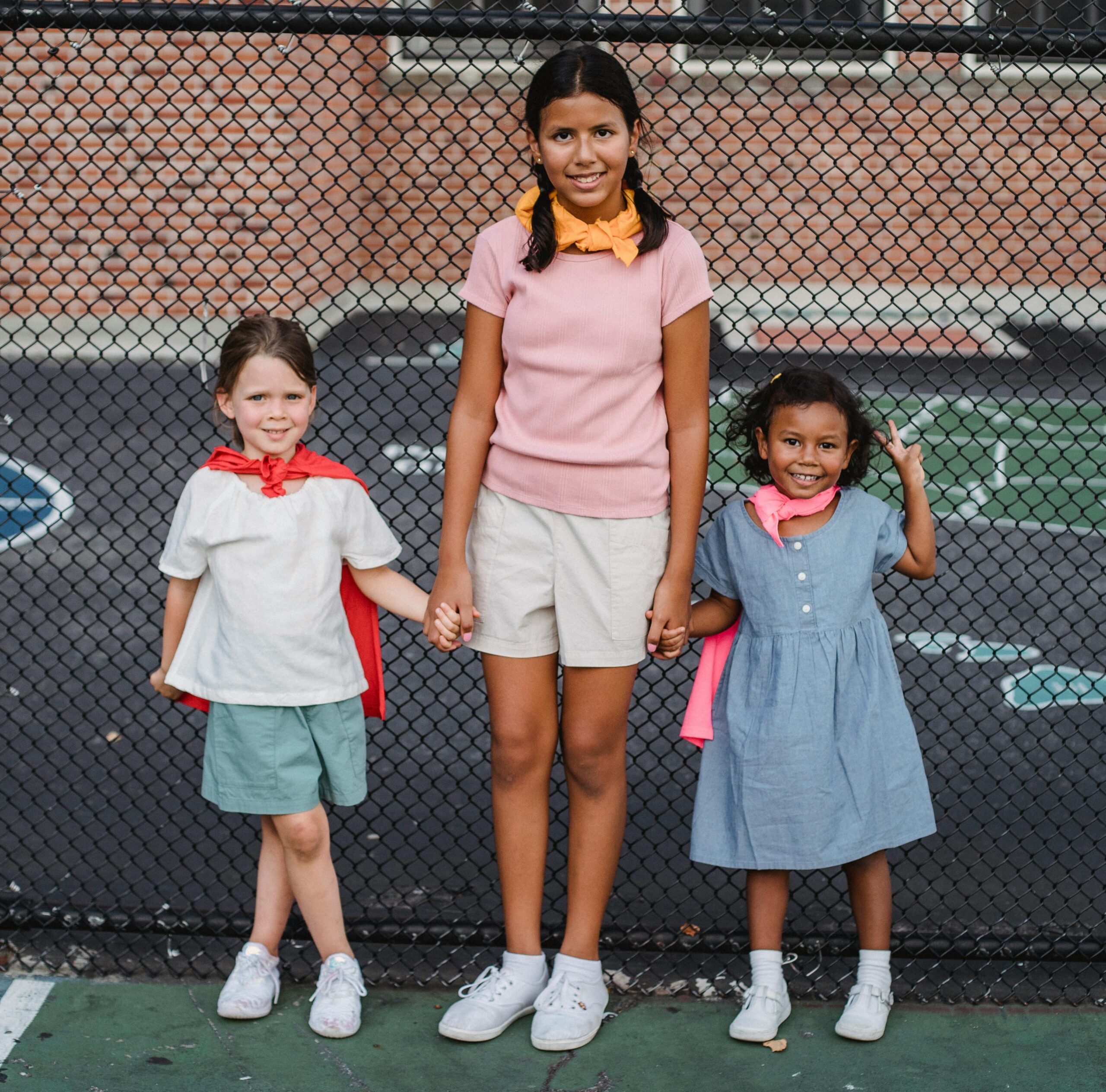 Three young girls holding hands while leaning on a fence.