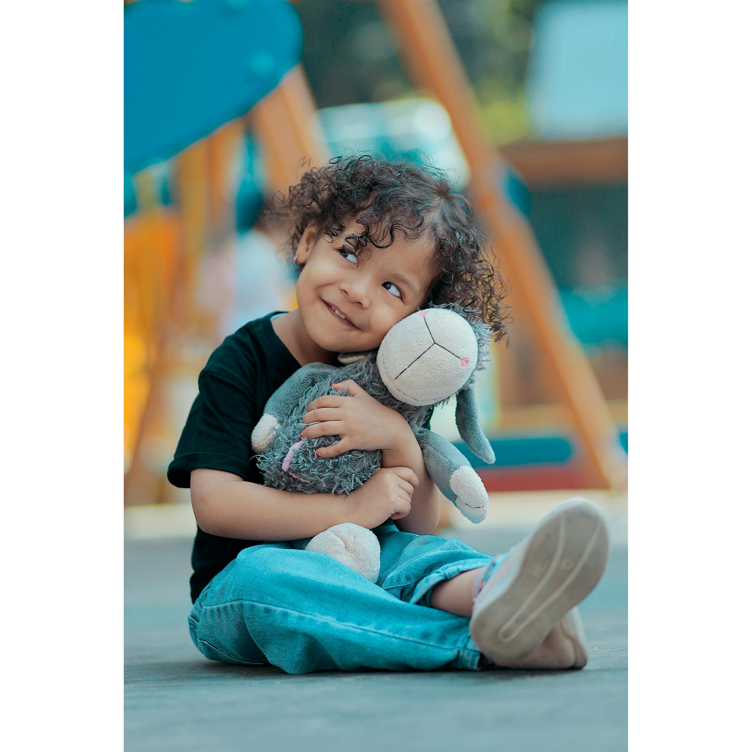 Menino sorrindo e abraçando seu bichinho de pelúcia no parquinho
