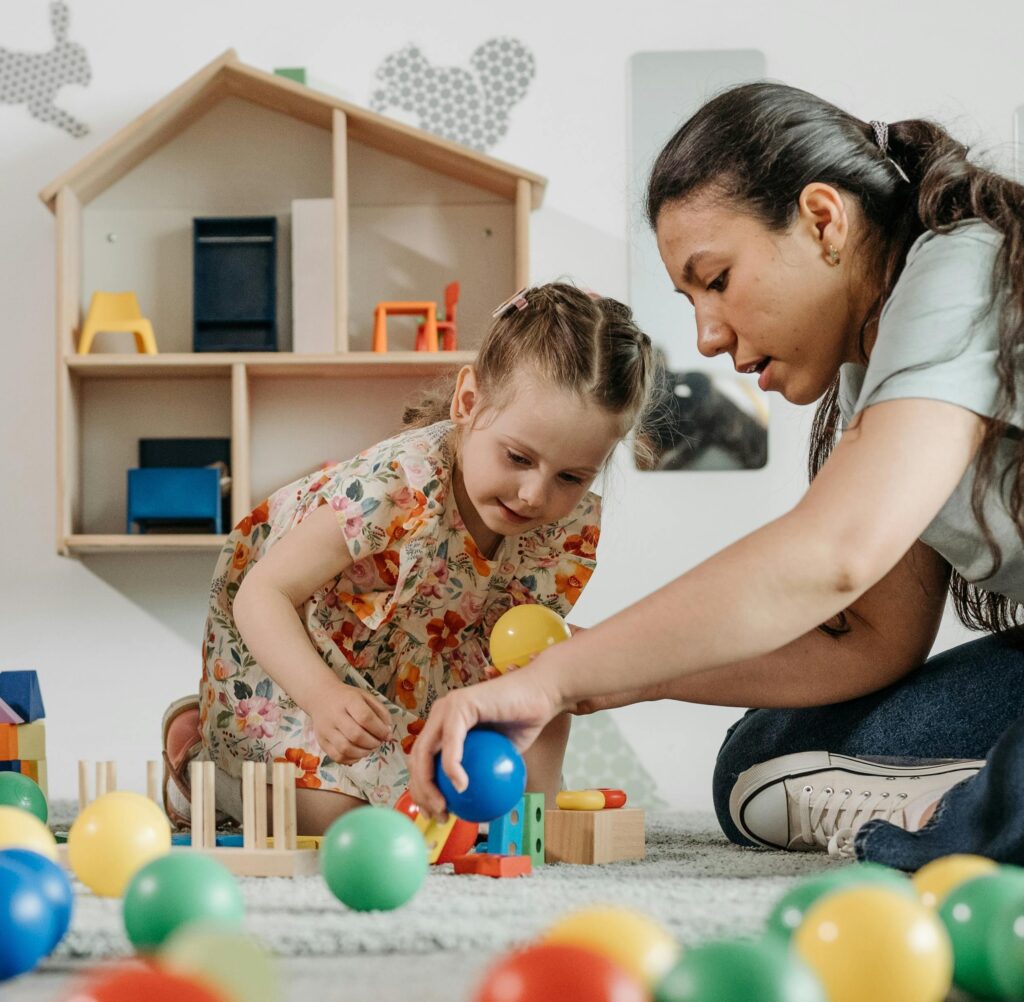 Child with adult playing with balls on the ground.
