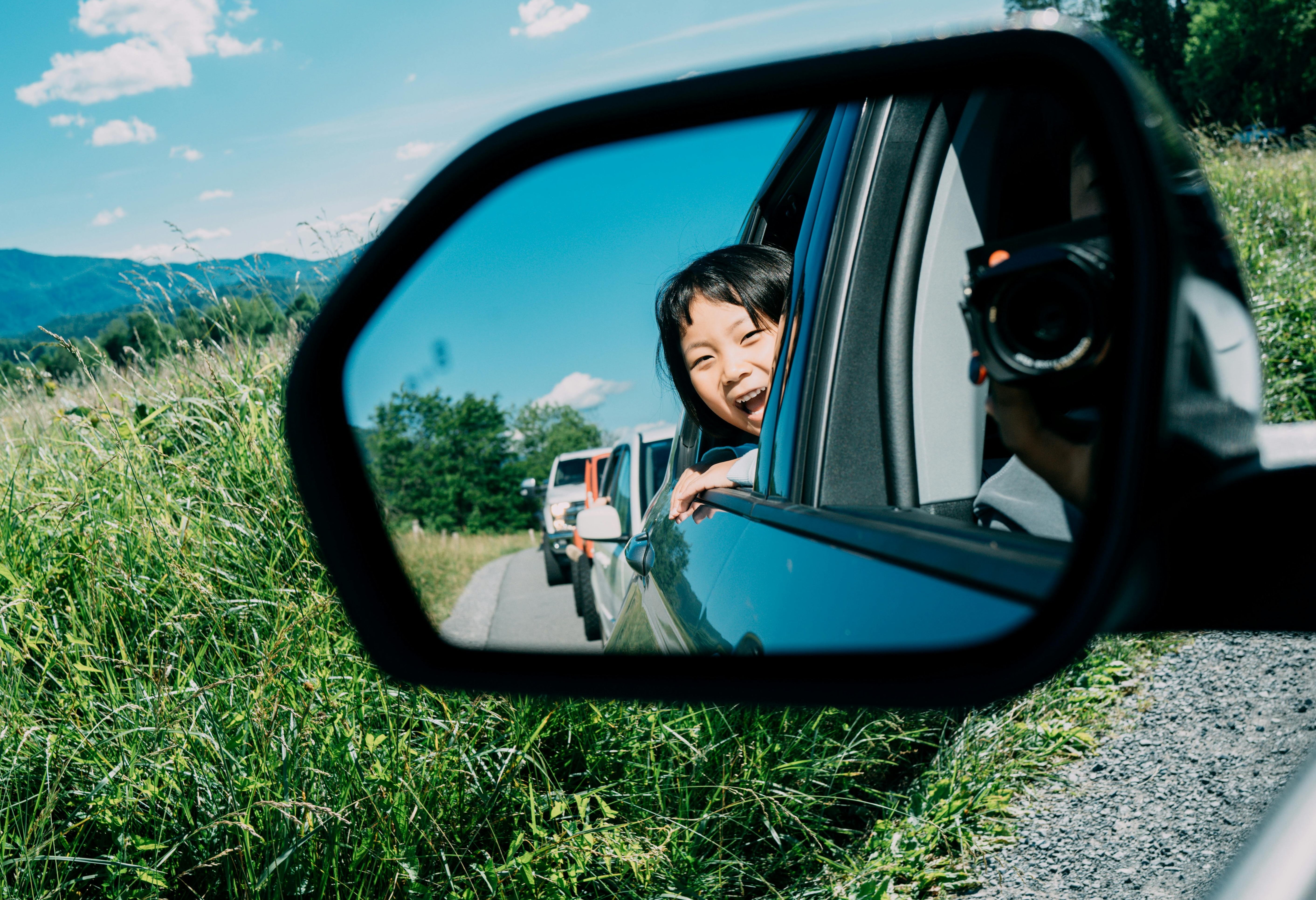 Girl reflecting in the side mirror of the car with mountains in the background