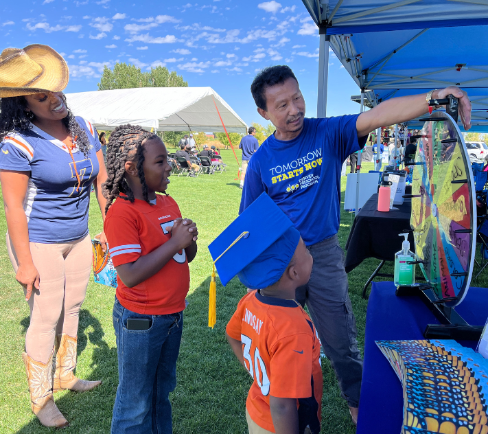 Children spinning a wheel for a prize; adults standing near by helping.