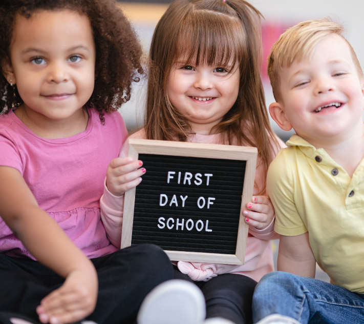 A girl, a girl, and a boy holding a back-to-school sign