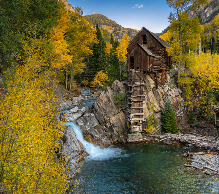 Wooden cabin by stream and trees with fall colors