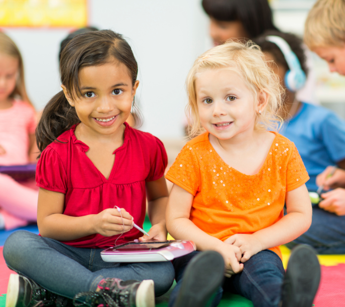 Two young girls smiling with a notepad in their laps