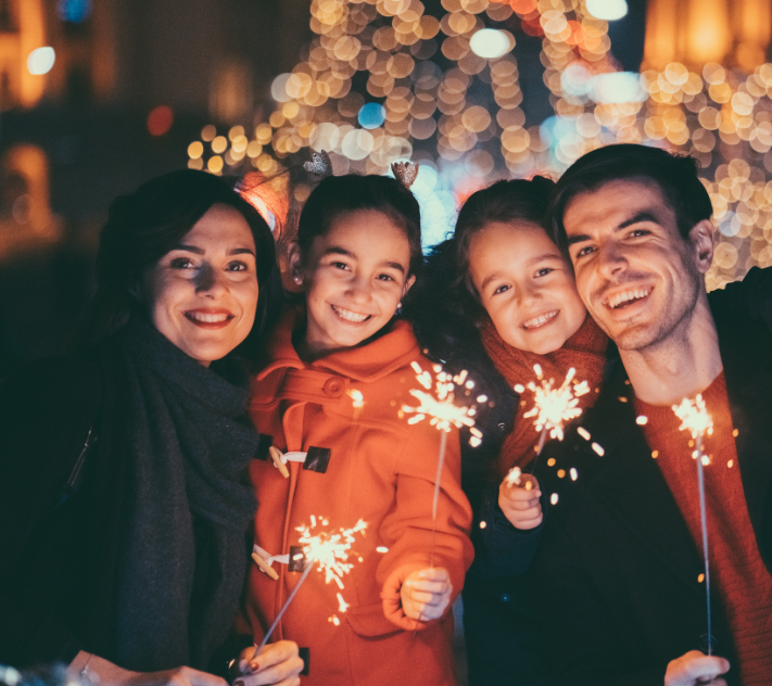 Mãe, filhas e pai sorrindo com velas de faísca.