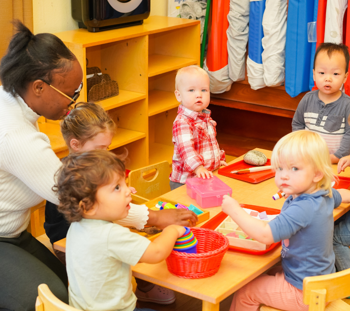 Teacher and young children sitting around a table doing art projects.