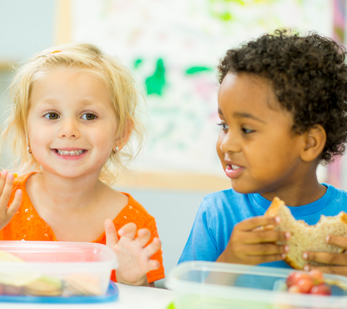 Junges Mädchen und Junge lächeln beim Essen von nussfreien Snacks.