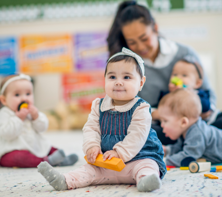 Young toddler girl with block in her hand sitting on a rug smiling