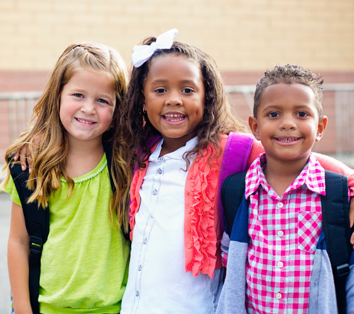 Three young children with backpacks standing next to each other.