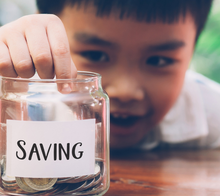 Young boy putting a coin in a jar that says "saving."