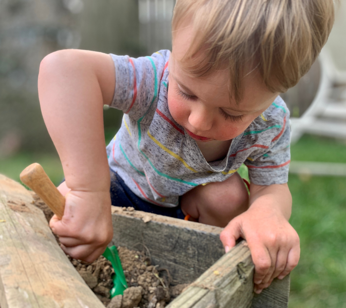 Un jeune garçon creuse la terre d'un bac à jardin avec une petite pelle.
