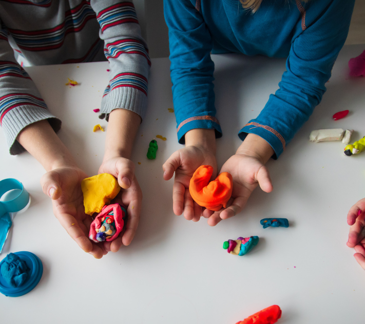 Crianças pequenas (apenas as mãos visíveis) brincando de modelagem em uma pré-escola baseada em brincadeiras.