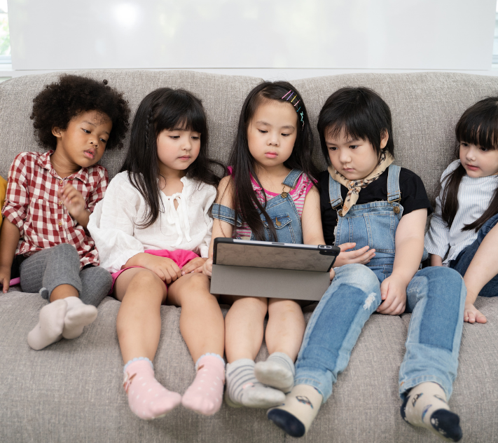Young children sitting on the couch watching a show on a tablet.
