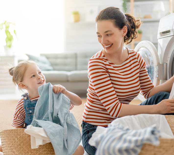 Young girl and her mother sitting on the floor sorting laundry while smiling at each other.